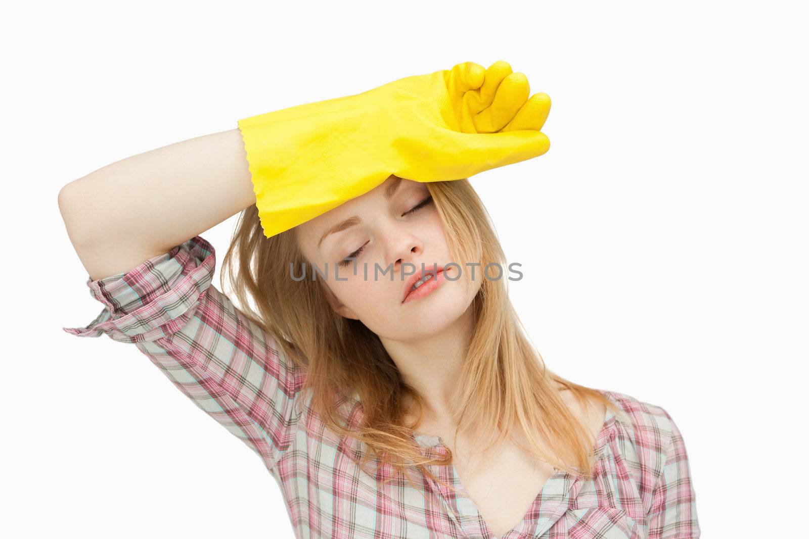 Woman wearing cleaning gloves while wiping her brow against white background