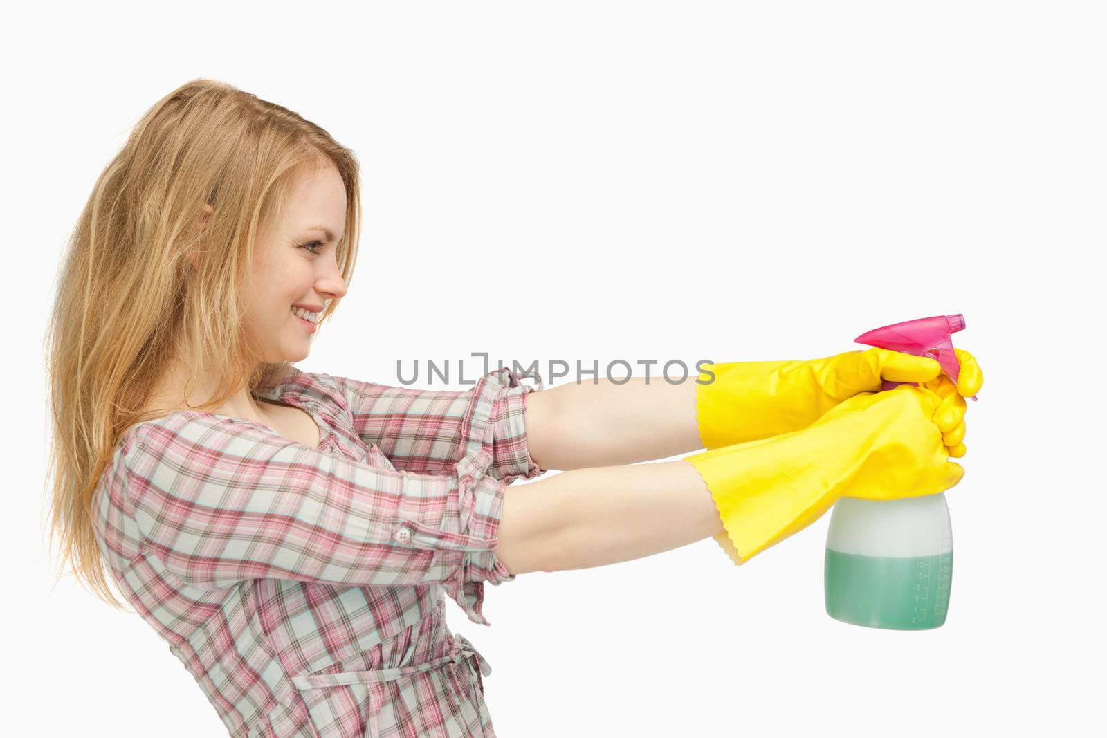 Fair-haired woman holding a spray bottle while smiling against white background