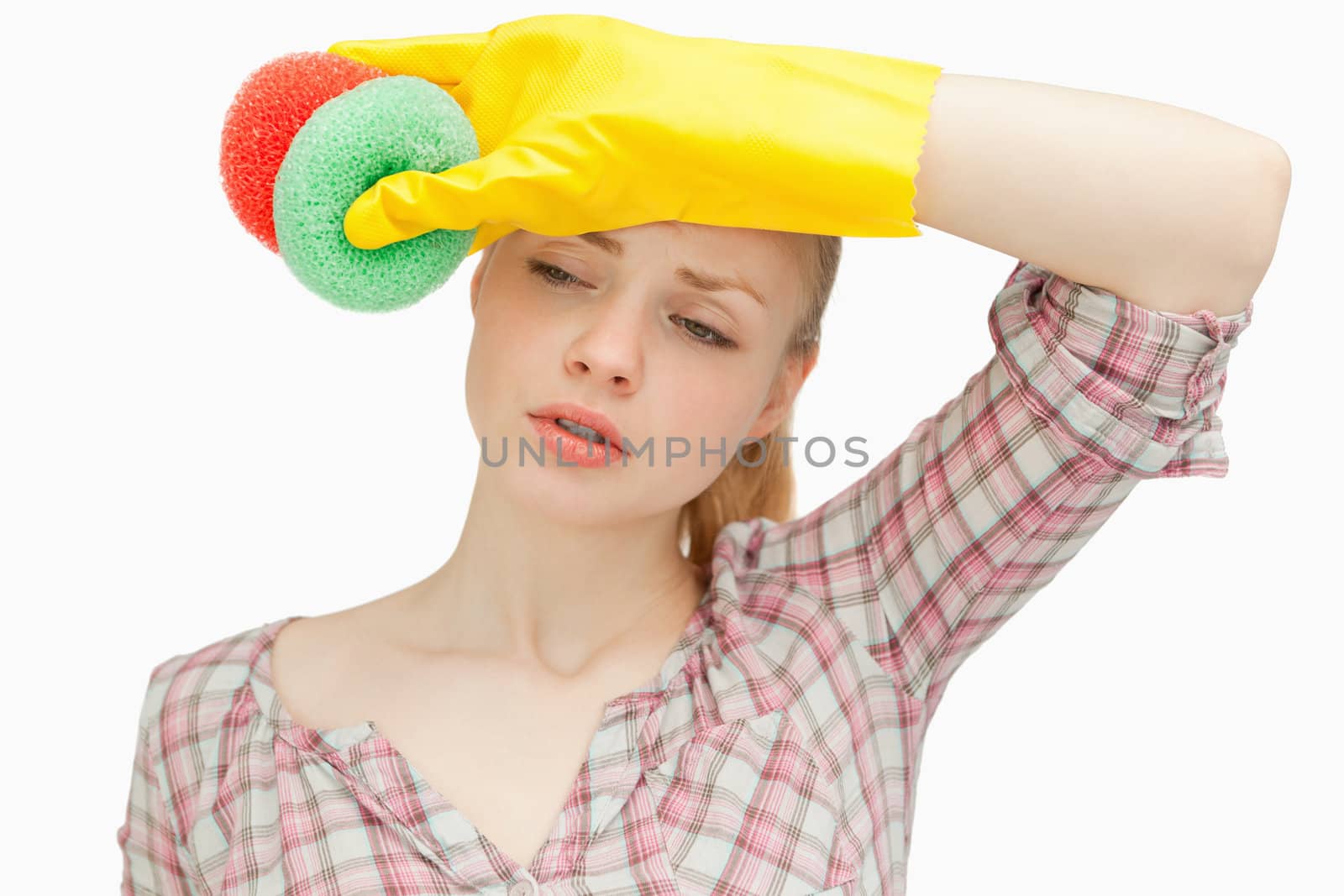 Woman wiping her forehead while holding sponges against white background