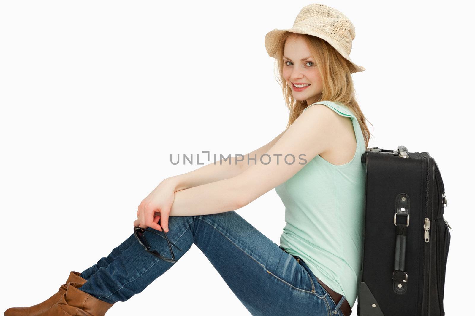 Joyful woman sitting near a suitcase against white background