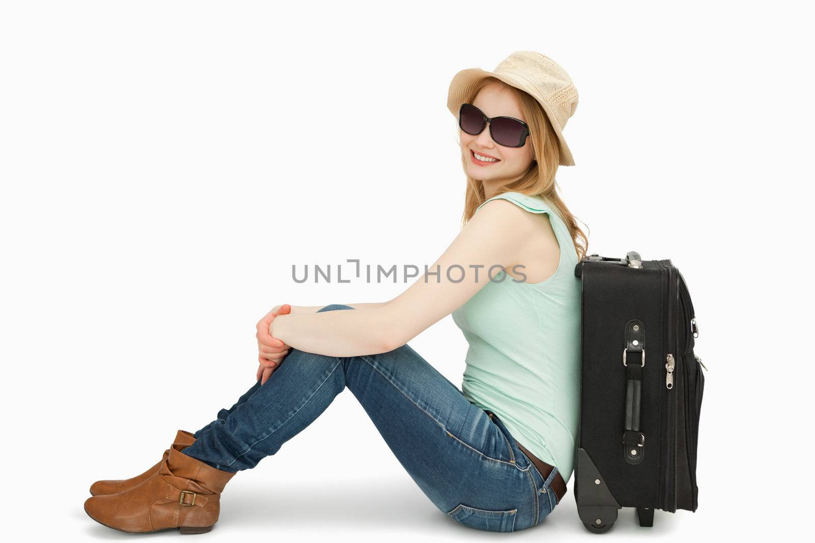 Woman wearing sunglasses while sitting near a suitcase against white background