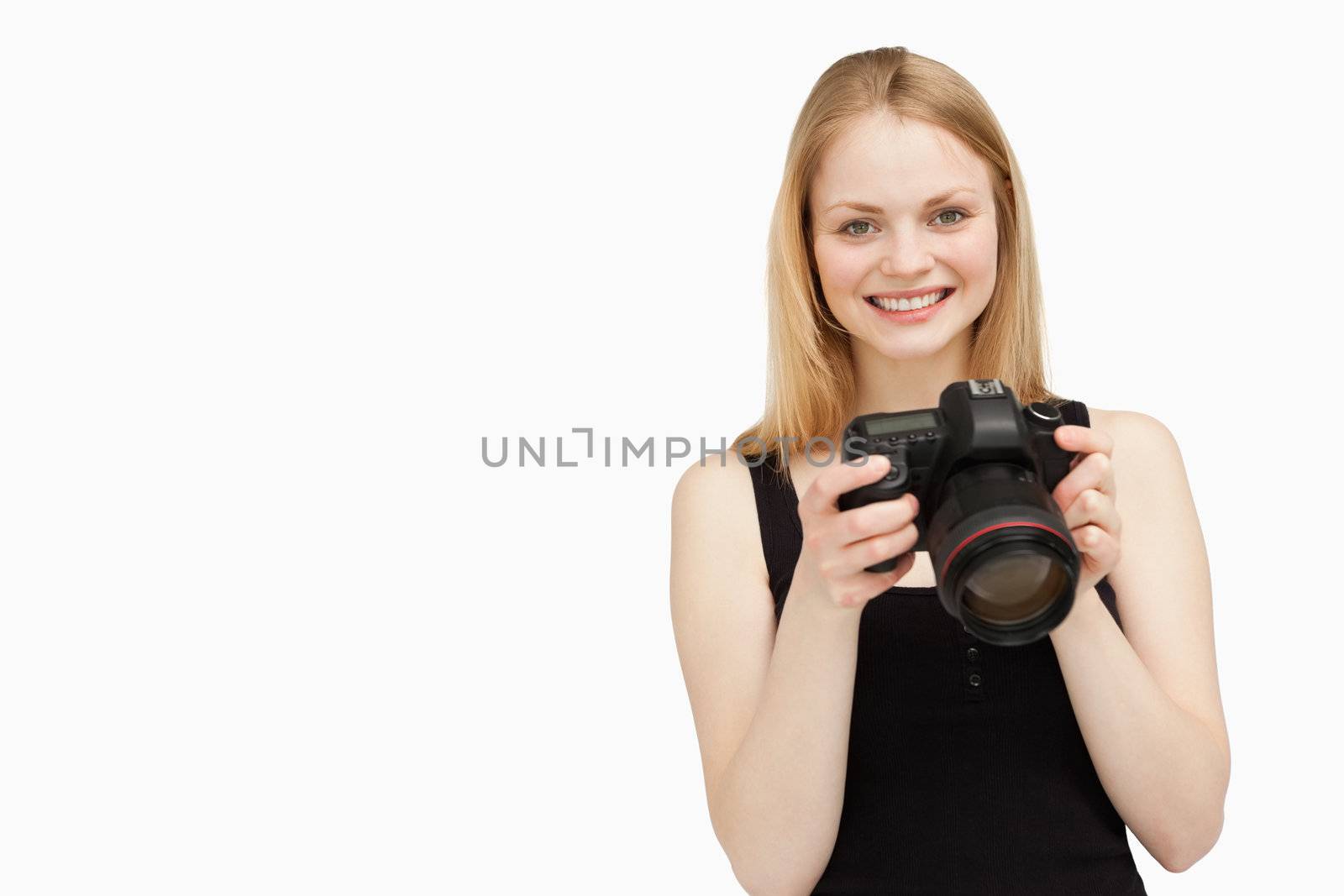 Woman holding a SLR camera while smiling against white background