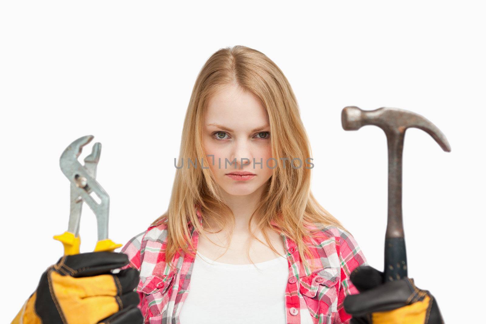 Serious woman holding a hammer and and a wrench against white background