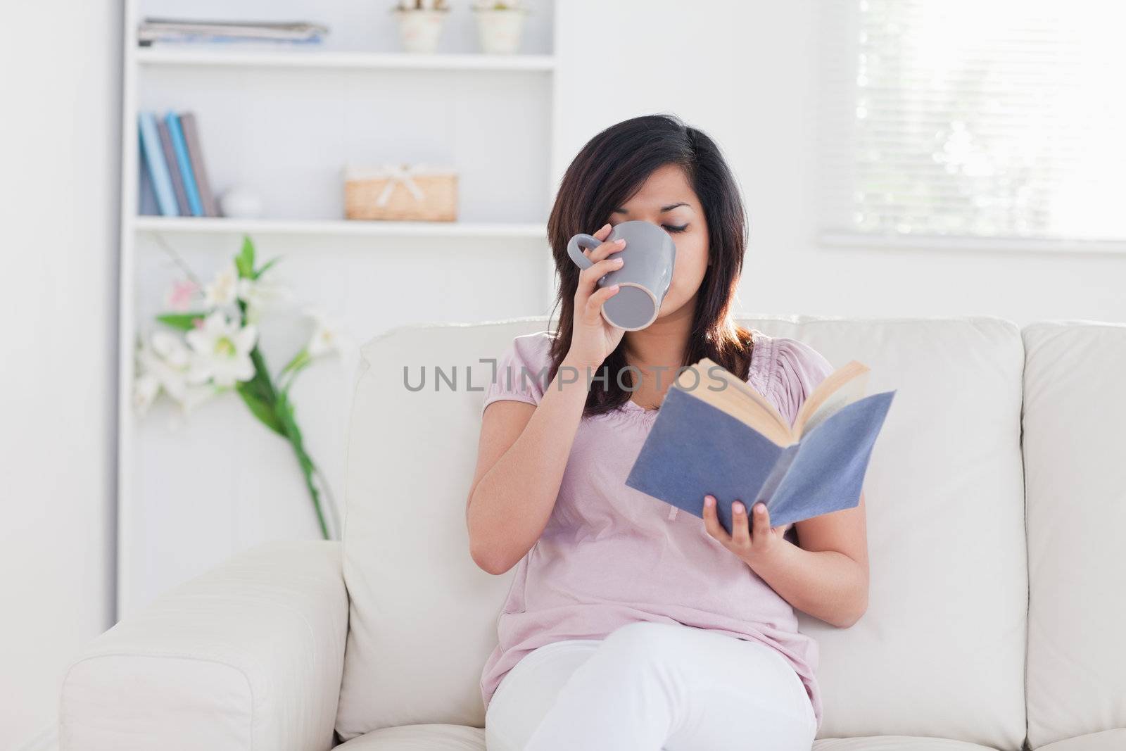 Woman holding a book and drinking in a living room