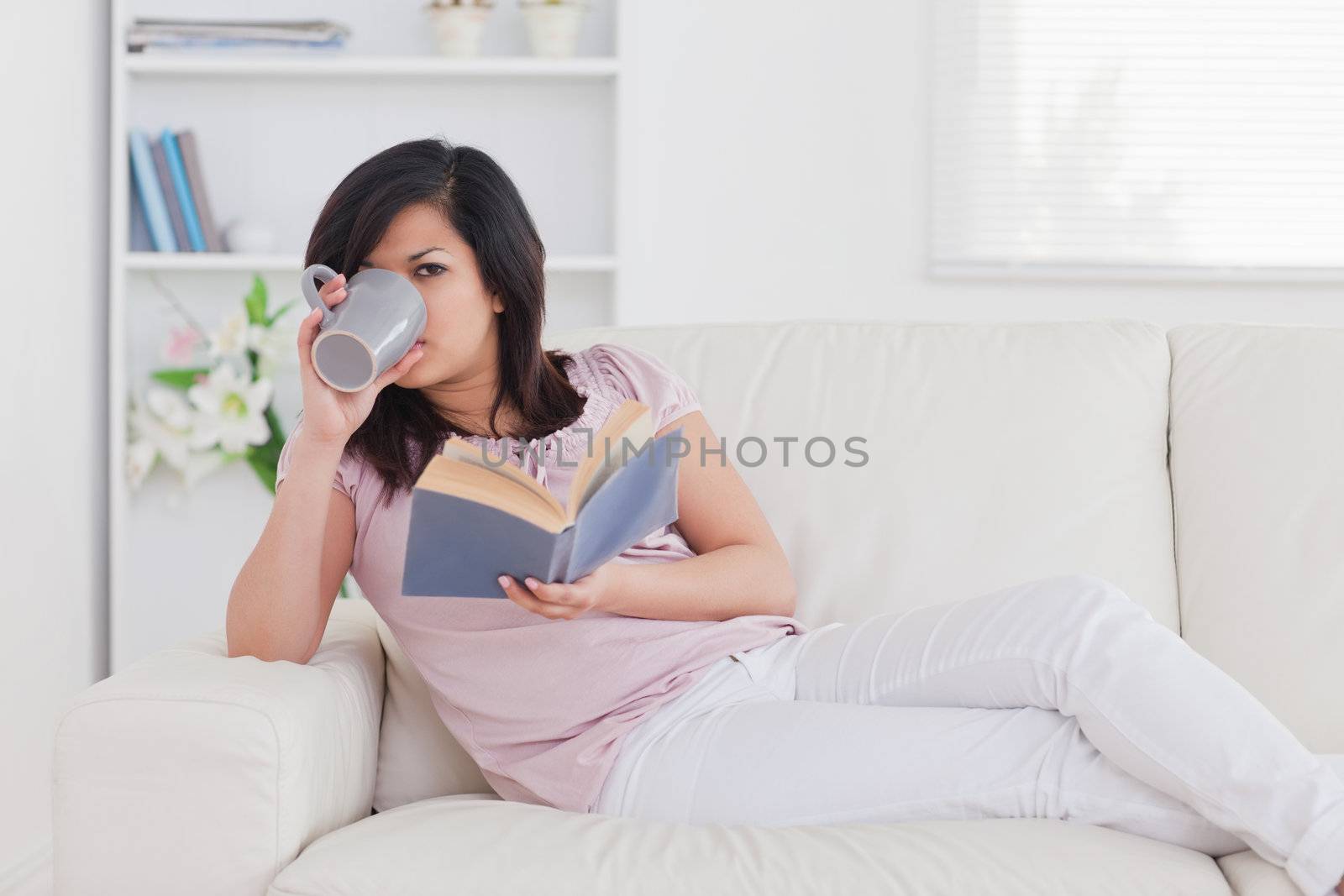 Woman drinking from a mug while lying on a sofa in a living room