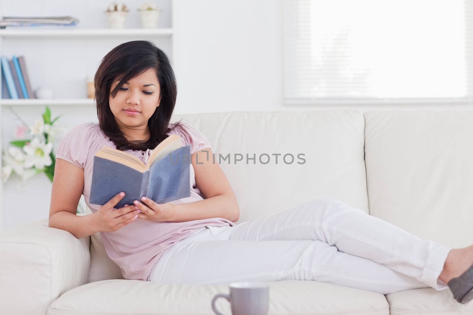 Woman reading a book while lying on a sofa in a living room