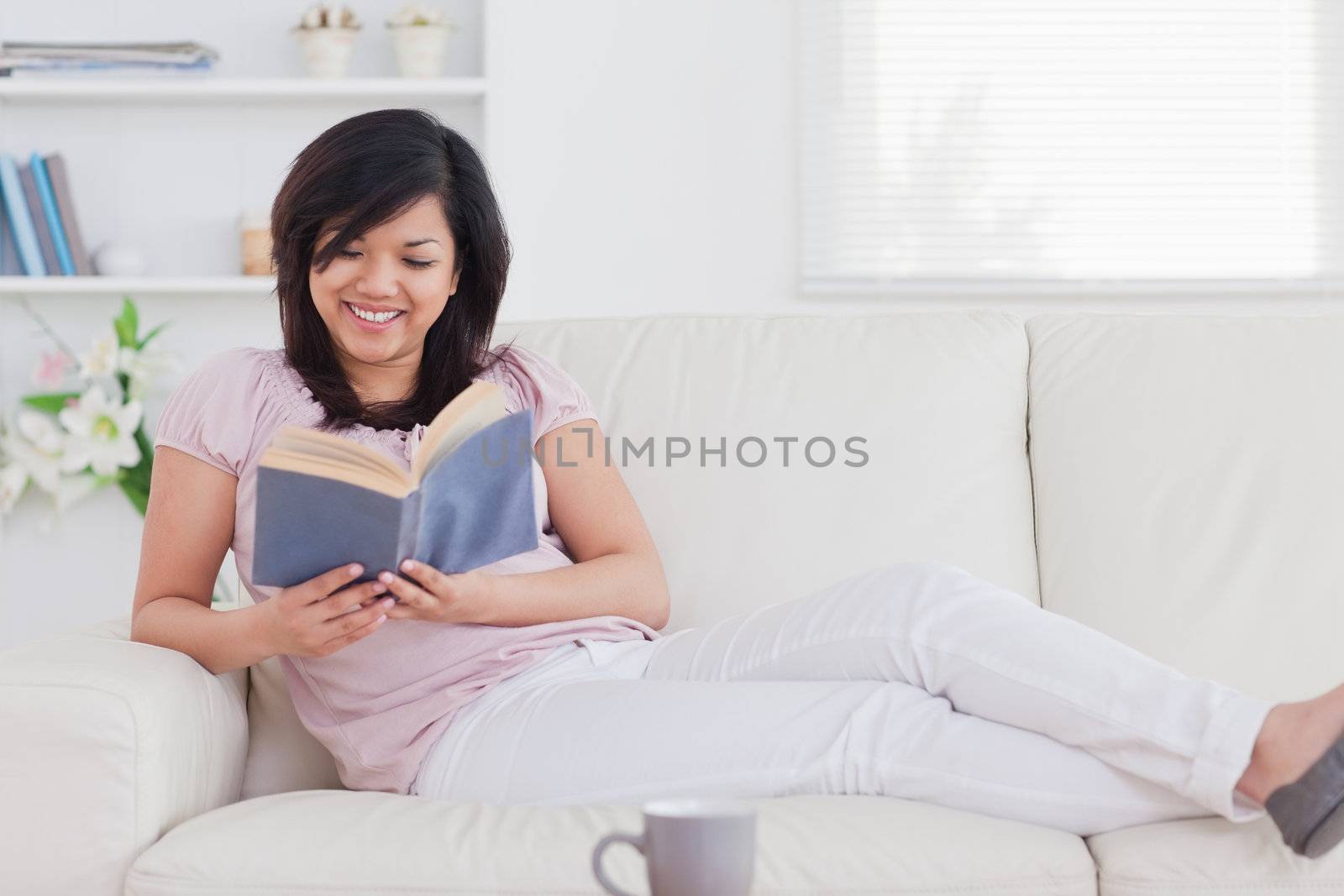 Woman reading a book while lying on a sofa in a living room