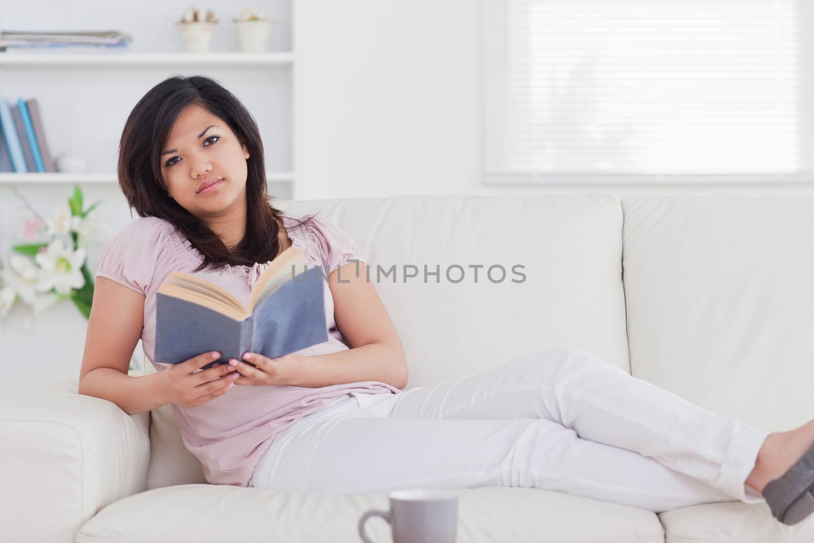 Woman lying on a couch while holding a book in a living room