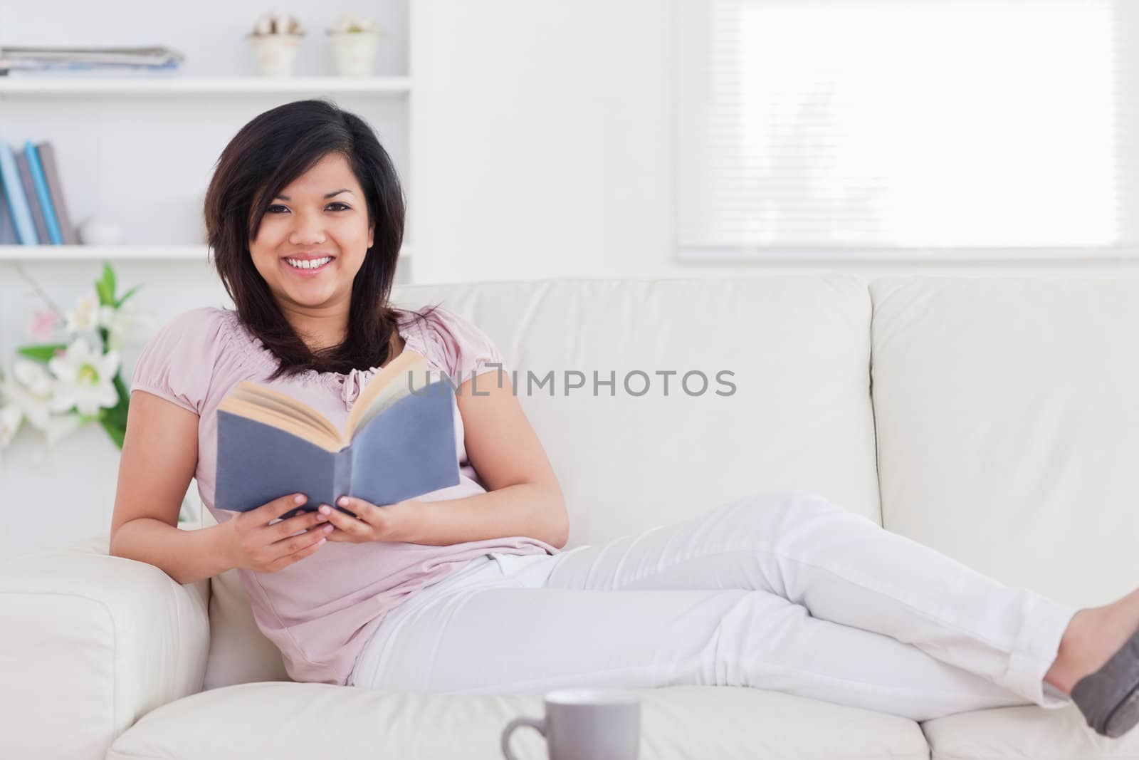 Woman lying on a sofa and holding a book in a living room