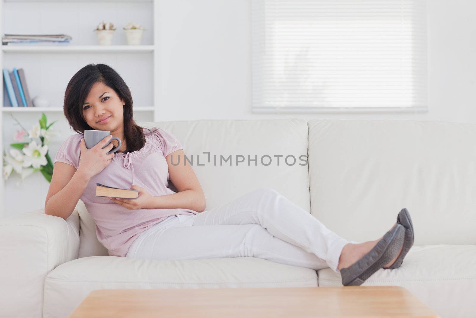 Woman sitting on a couch while holding a mug and a book in a living room