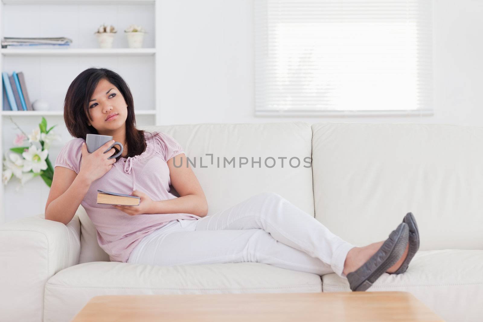 Woman thinking while holding a mug and a book in a living room