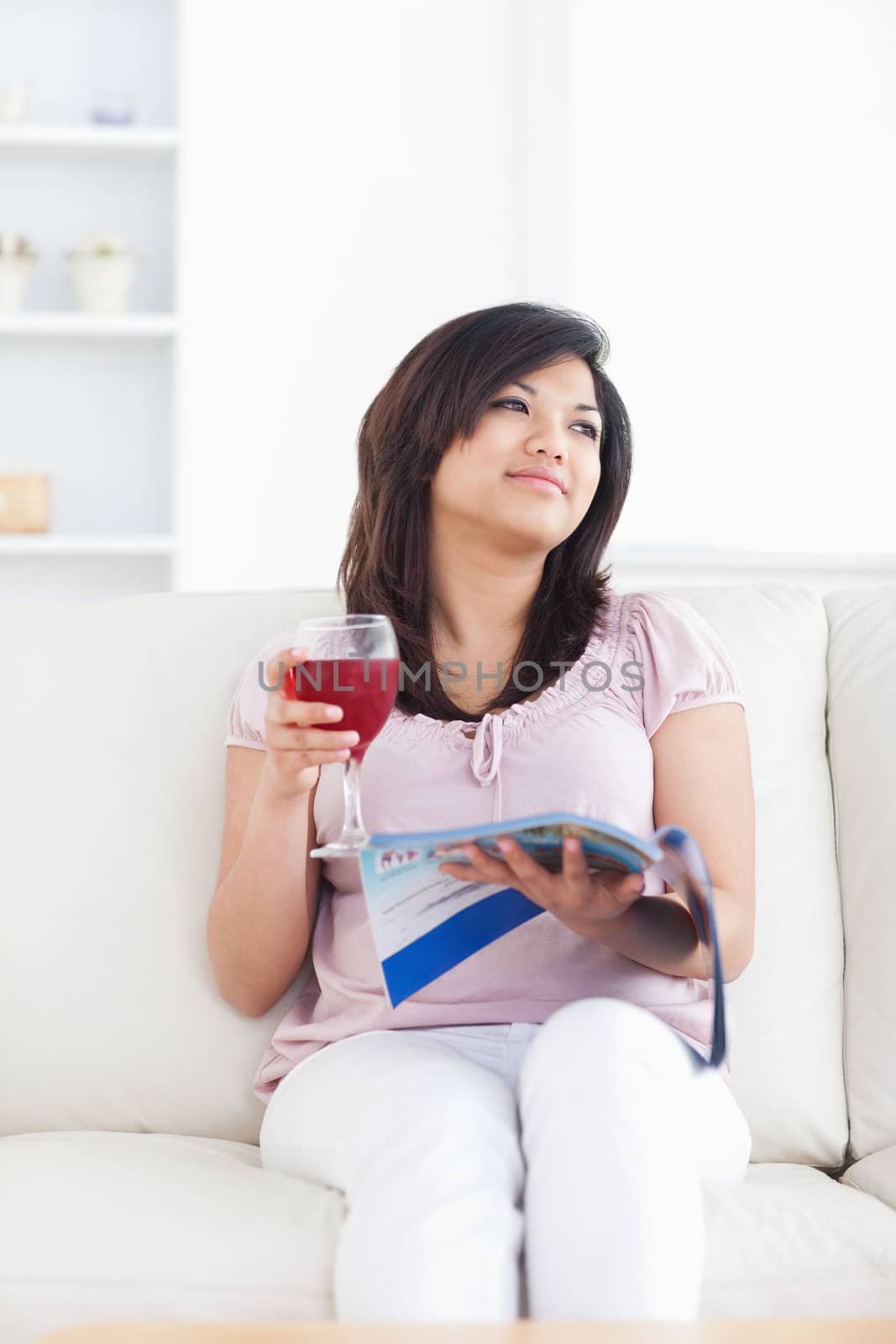 Woman sitting on a couch while holding a glass of red wine and a magazine in a living room