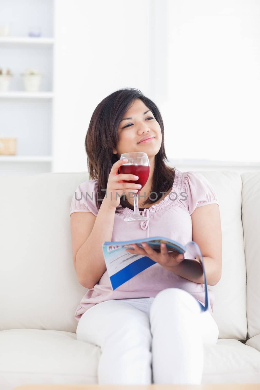 Woman smiling while sitting on a sofa and holding a glass of wine in a living room