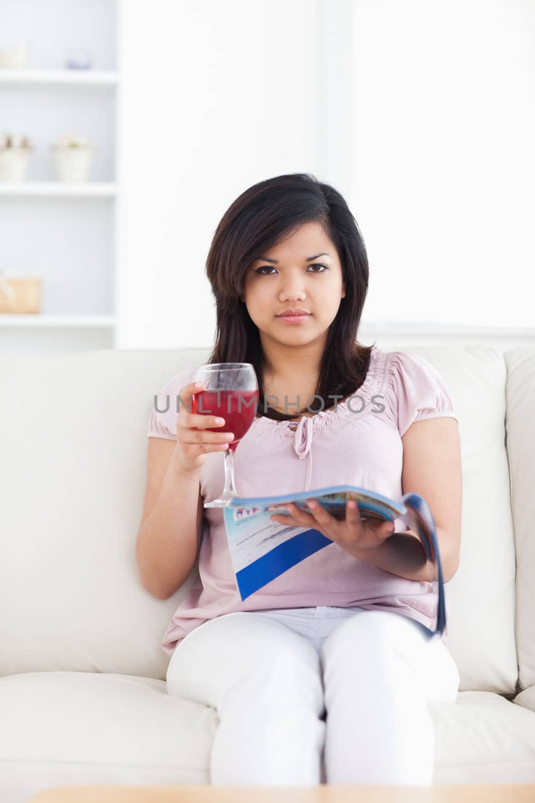 Woman holding a red glass of wine and a magazine in a living room