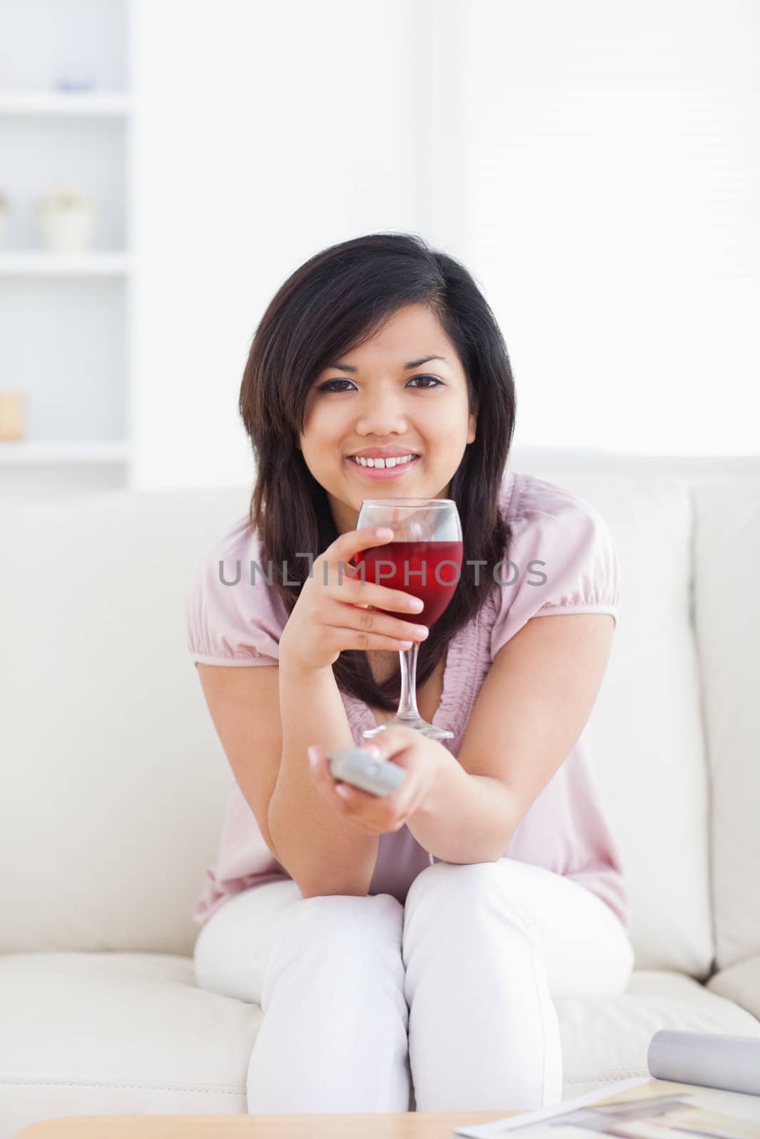Woman holding a television remote while holding a glass of red wine in a living room