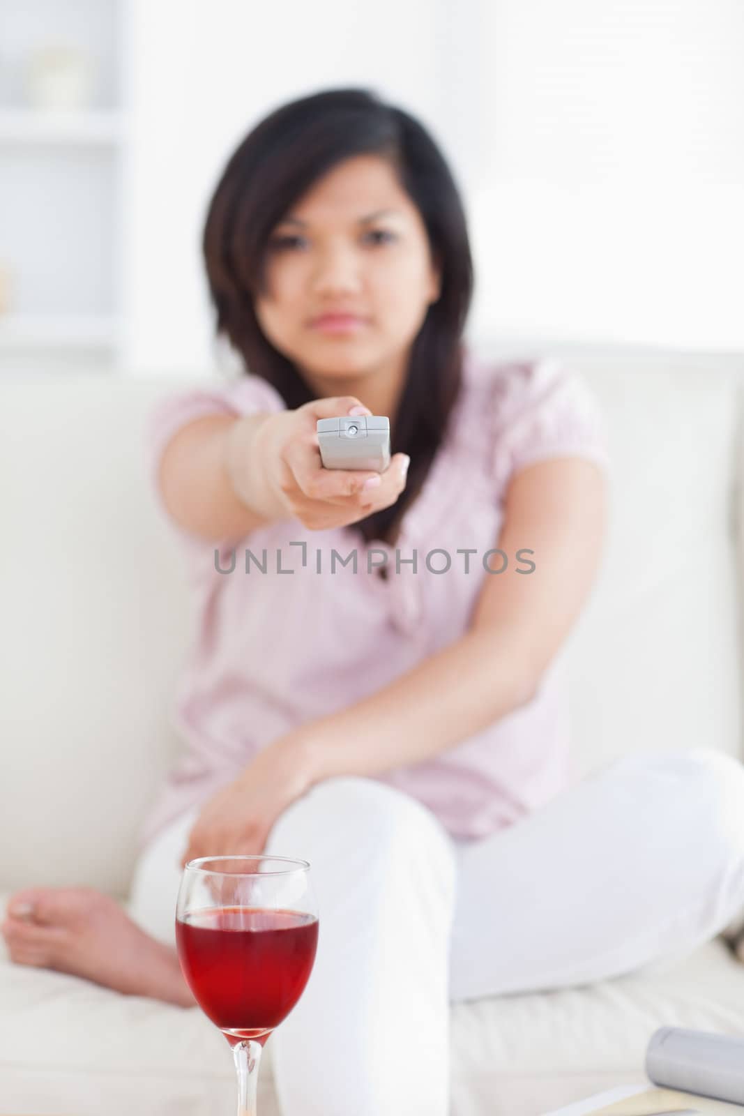 Woman holding a television remote in front of a glass of wine in a living room
