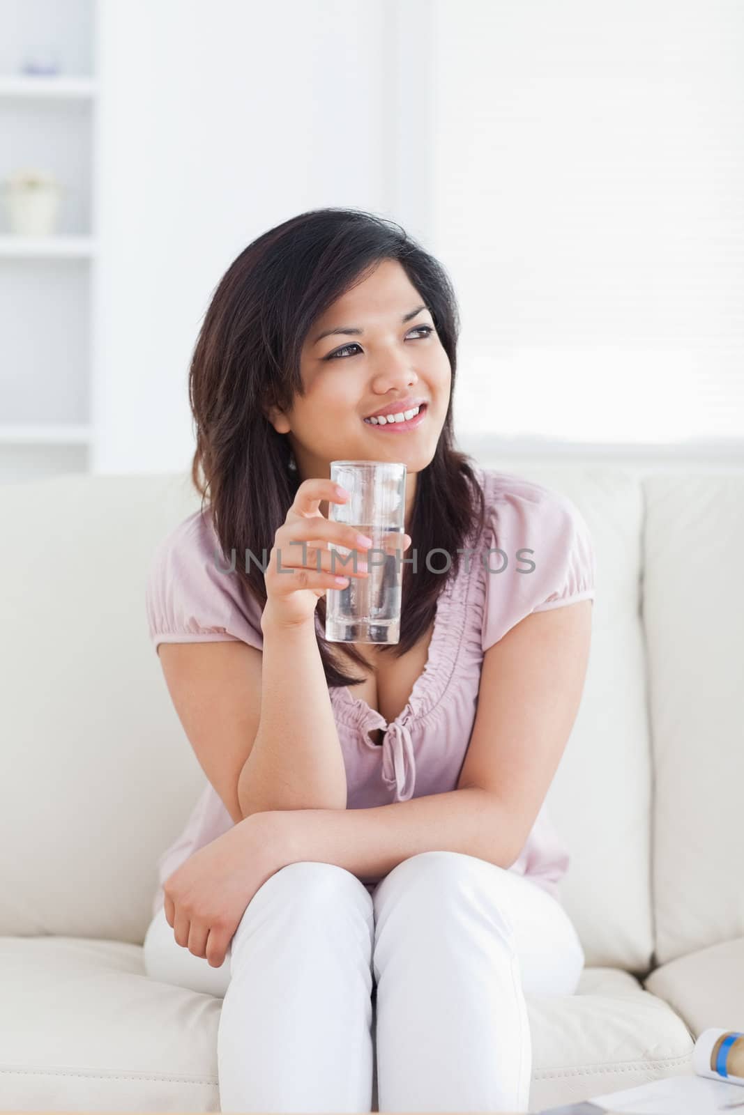 Woman sitting on a sofa and holding a glass of water in a living room