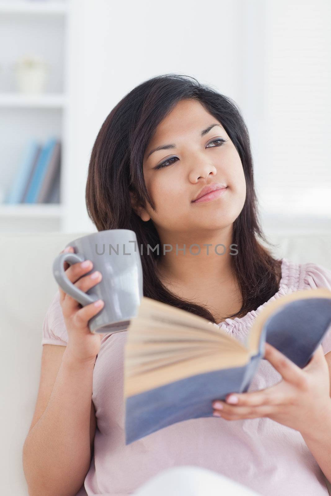 Woman sitting on a couch while holding a book and a mug in a living room