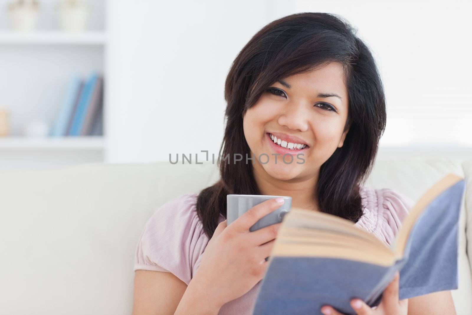 Woman with a mug and a book in her hands in the living room