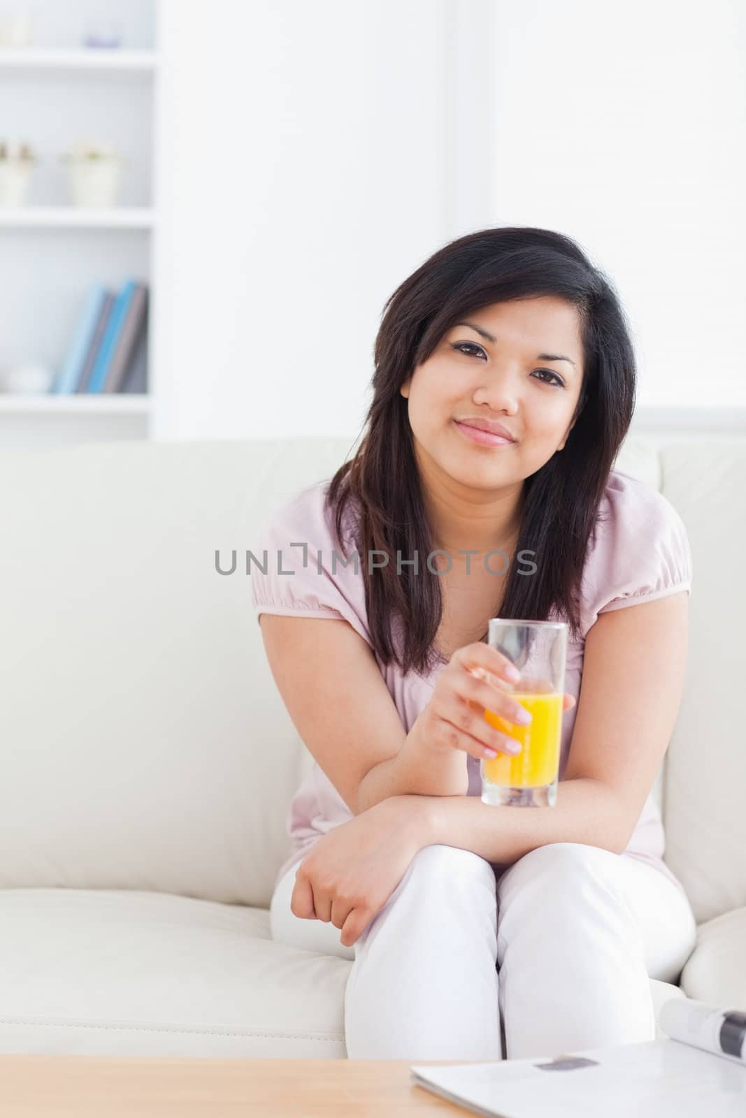 Woman sitting on a sofa while holding a glass of orange juice in a living room