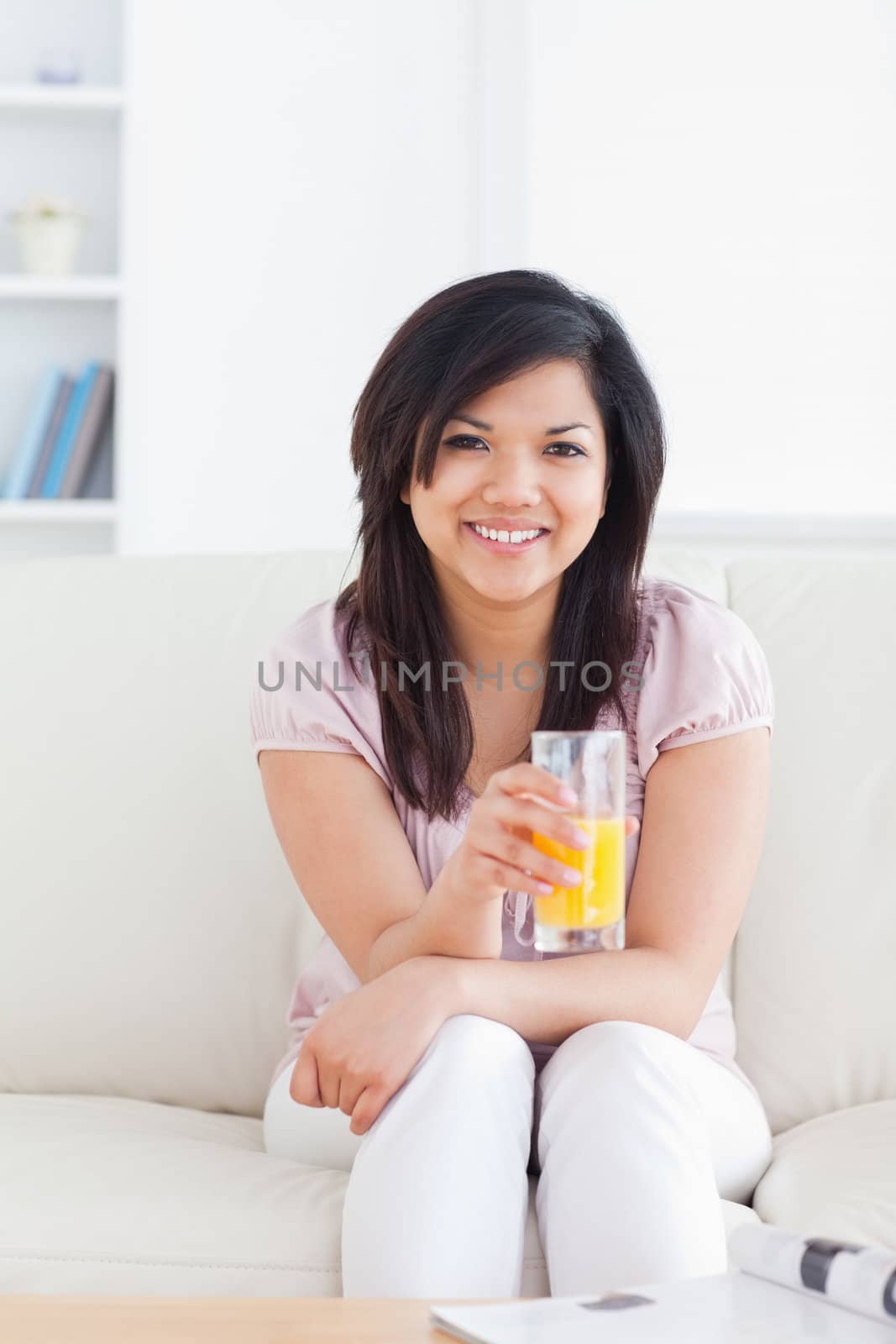 Smiling woman sitting and holding a glass of orange juice in a living room