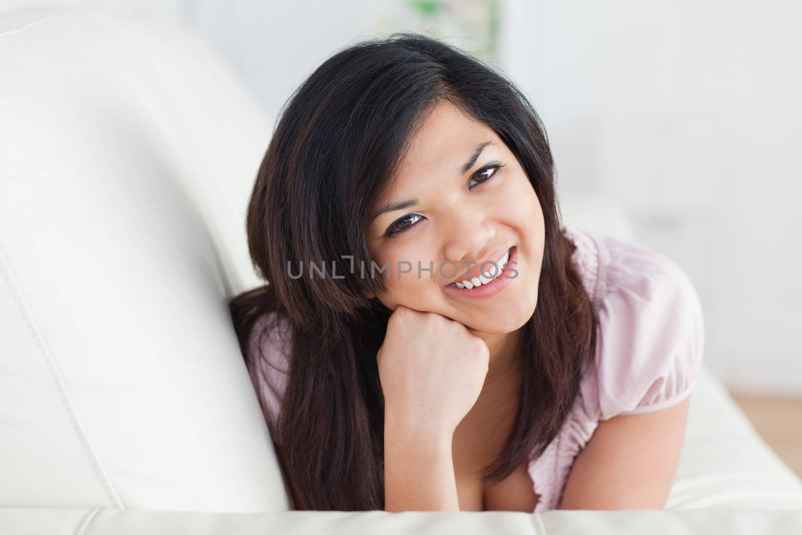 Smiling woman relaxing on a couch while holding her head with fist in a living room