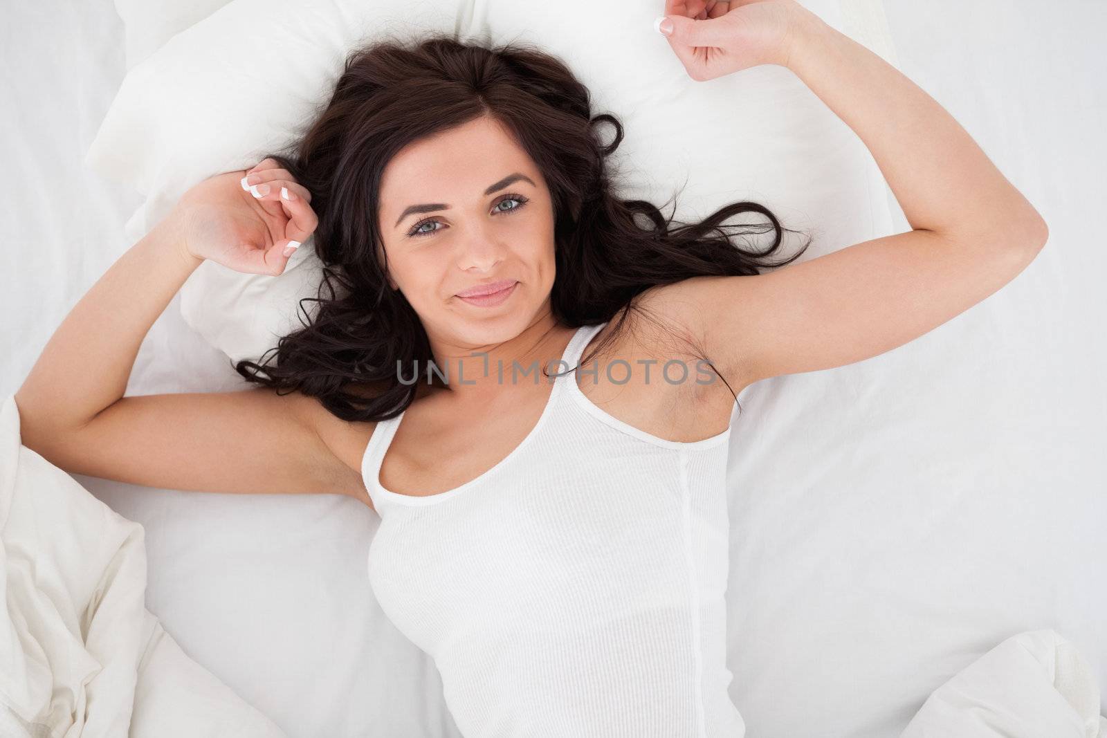Peaceful brunette woman stretching her body while lying in a bedroom