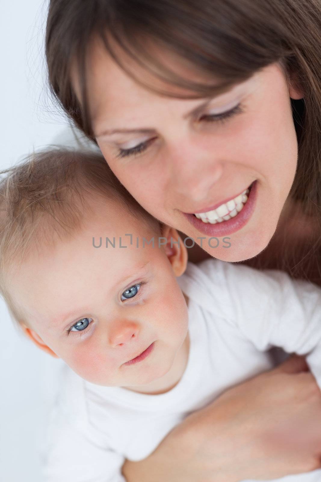 Cheerful mother holding her cute baby against a grey background