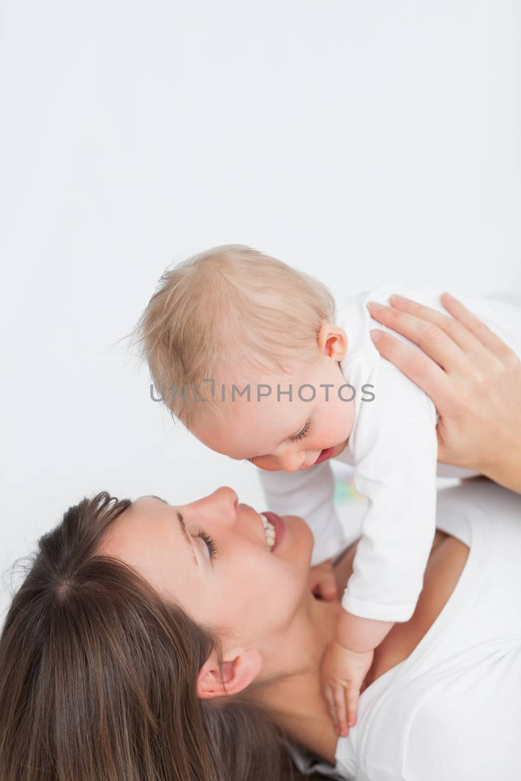 Smiling brunette woman playing with her baby against a grey background