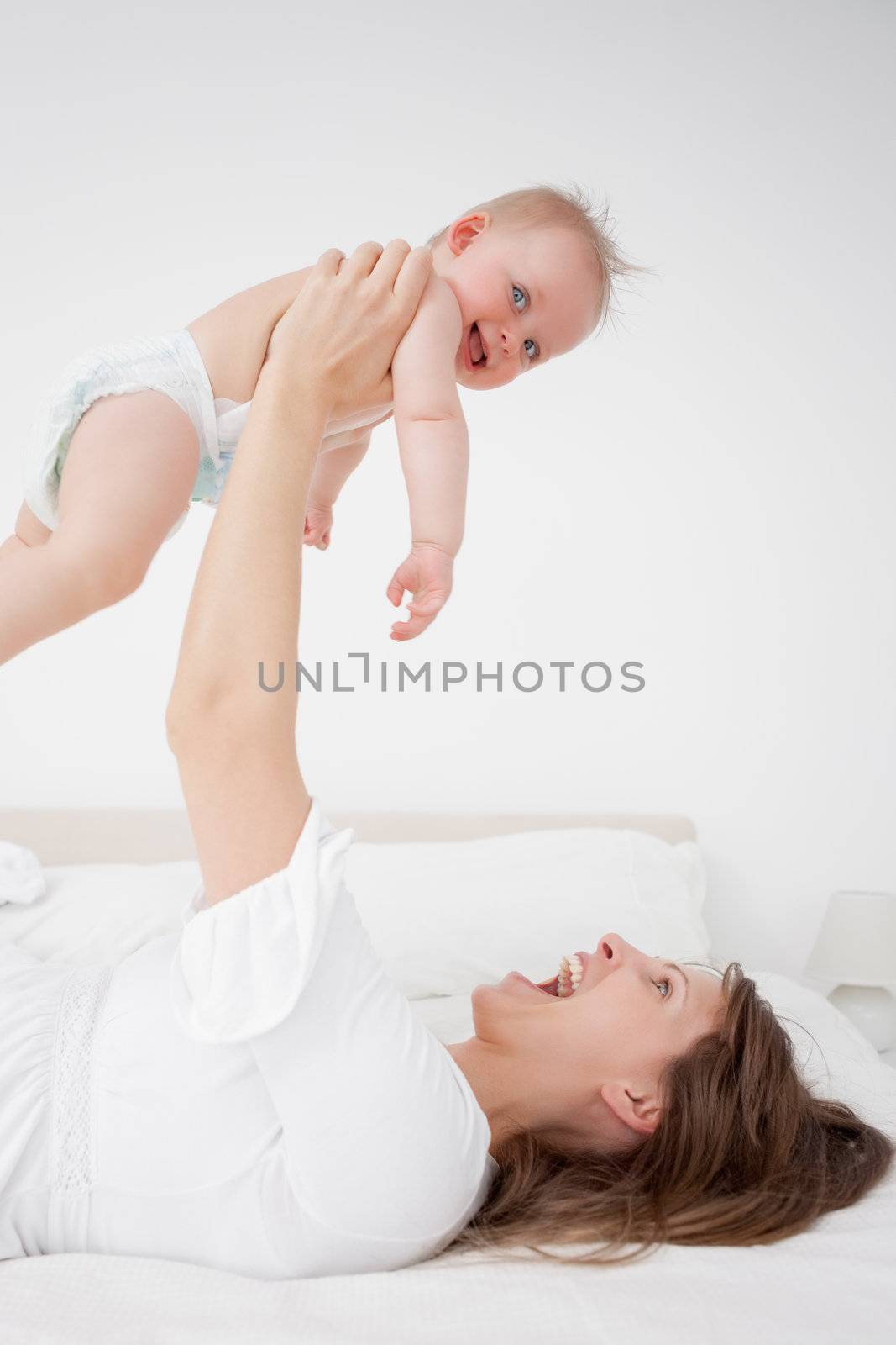 Happy woman holding her baby while lying in a bedroom