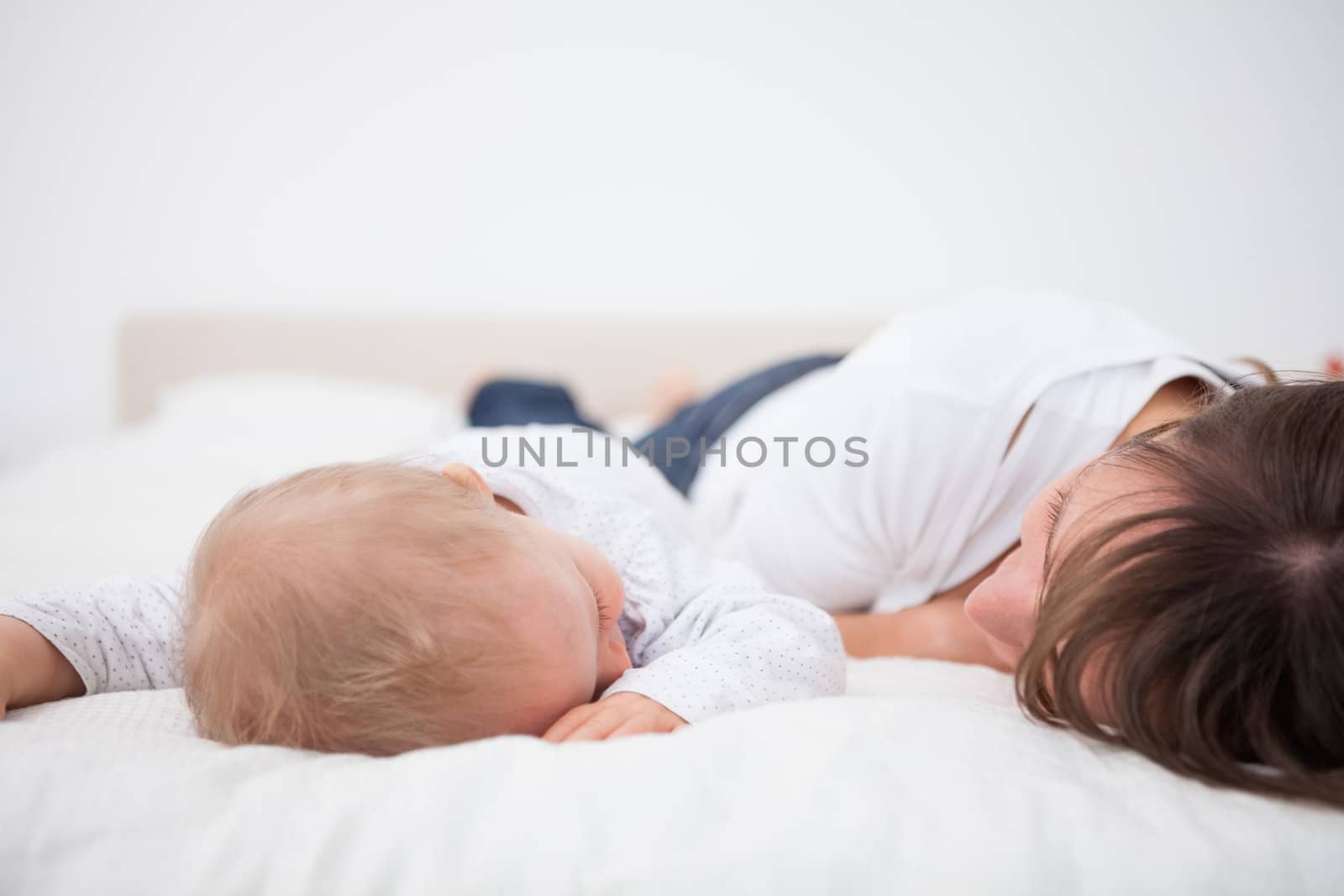 Brunette woman and her baby lying together in a bedroom