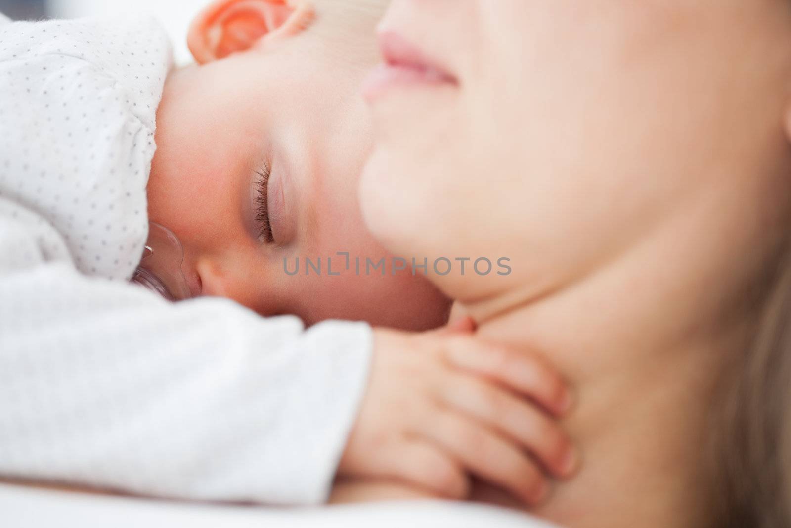 Cute baby sleeping on the chest of her mother indoors