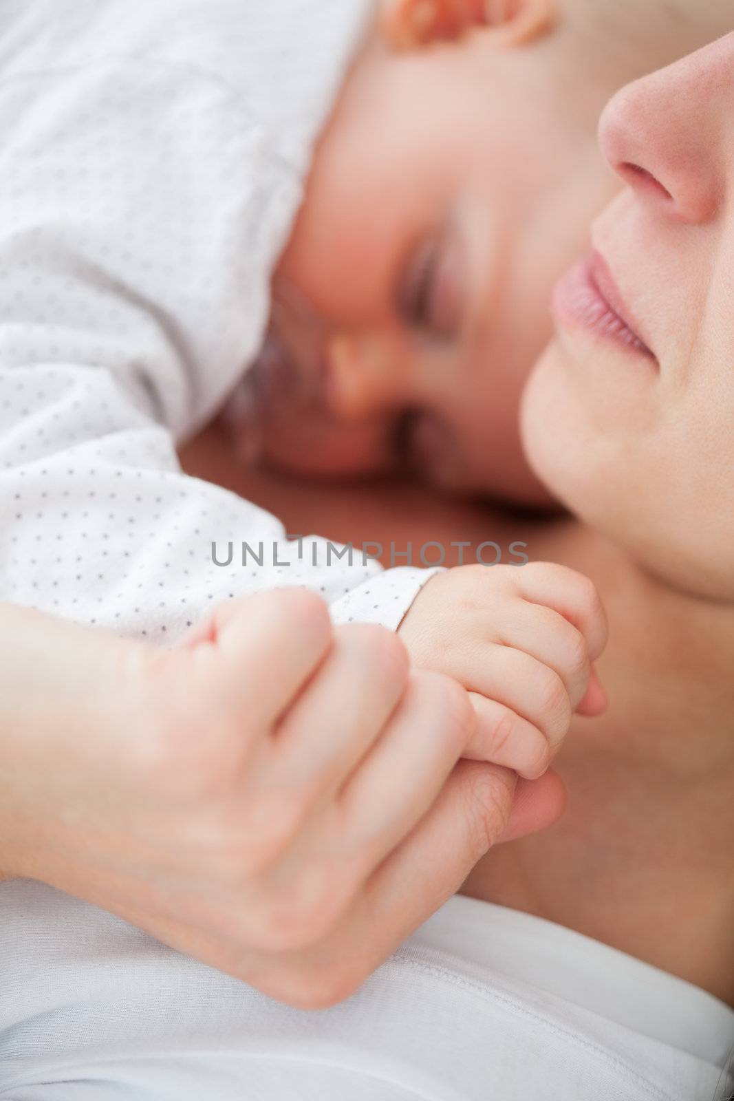 Peaceful woman lying with her baby who is sucking a pacifier indoors
