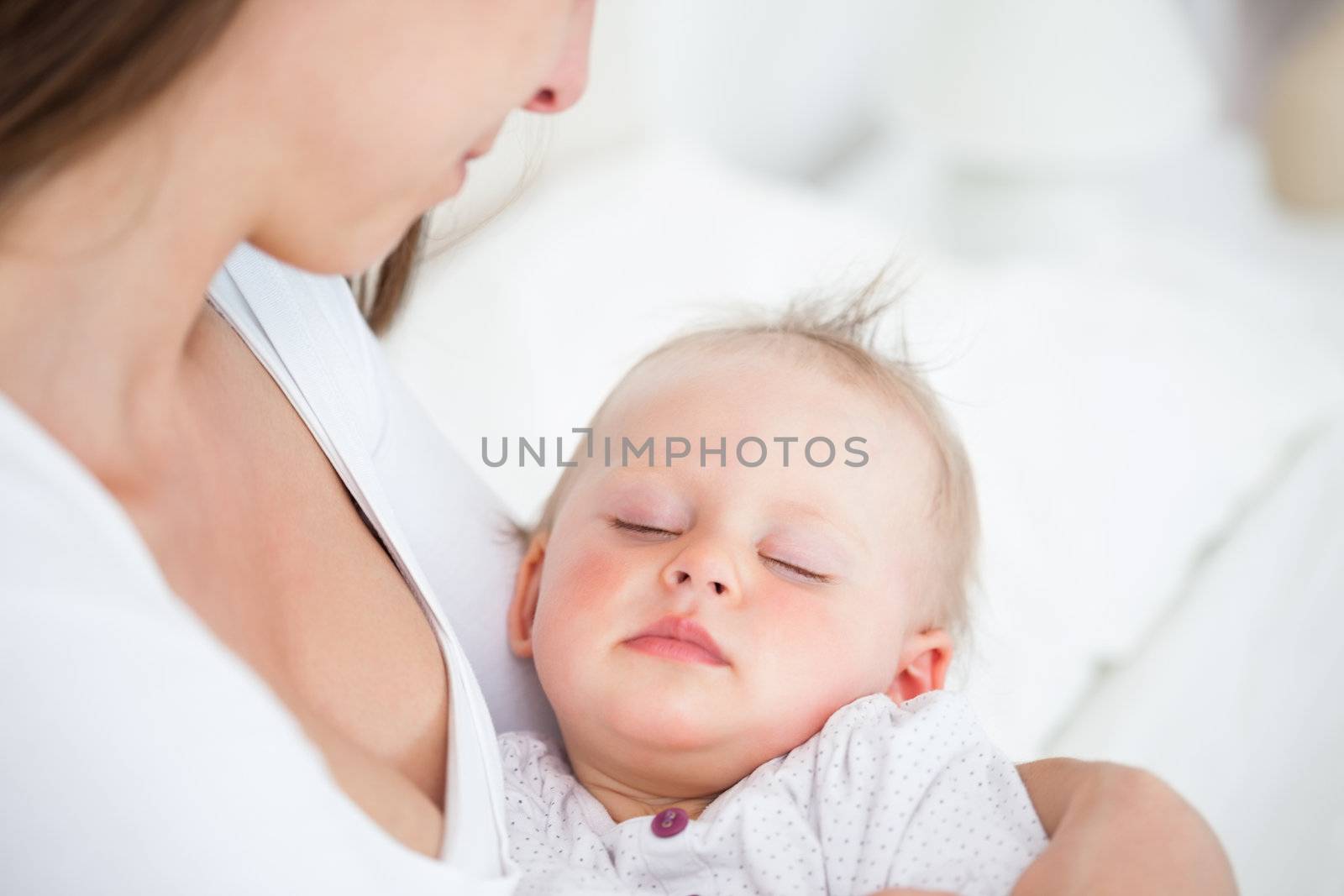 Baby falling asleep in the arms of her mother in a bedroom