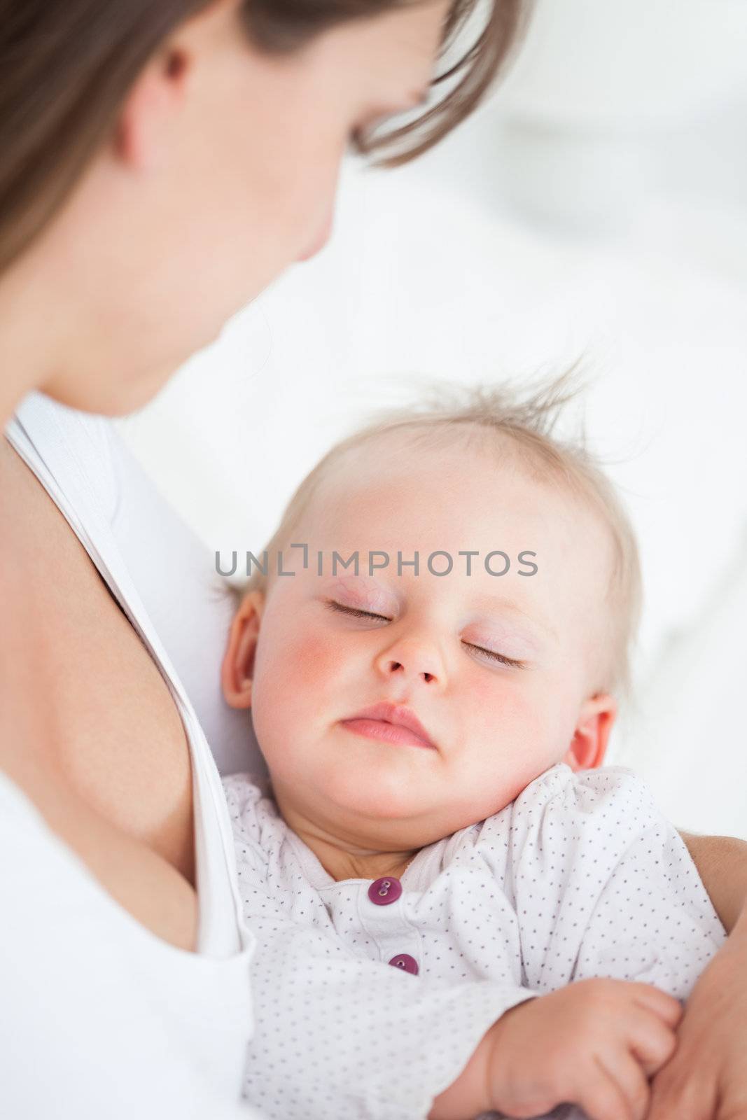 Cute baby sleeping in the arms of her mother in a bedroom