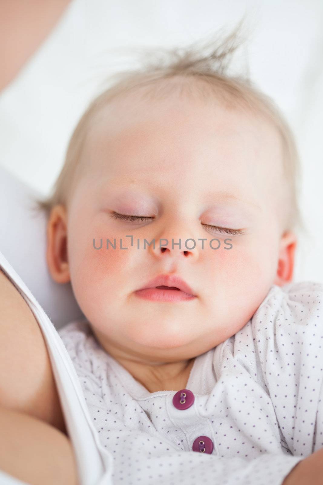 Beautiful baby sleeping in the arms of her mother by Wavebreakmedia