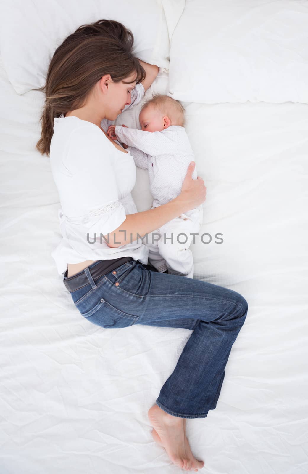 Brunette woman lying next to her baby in a bedroom