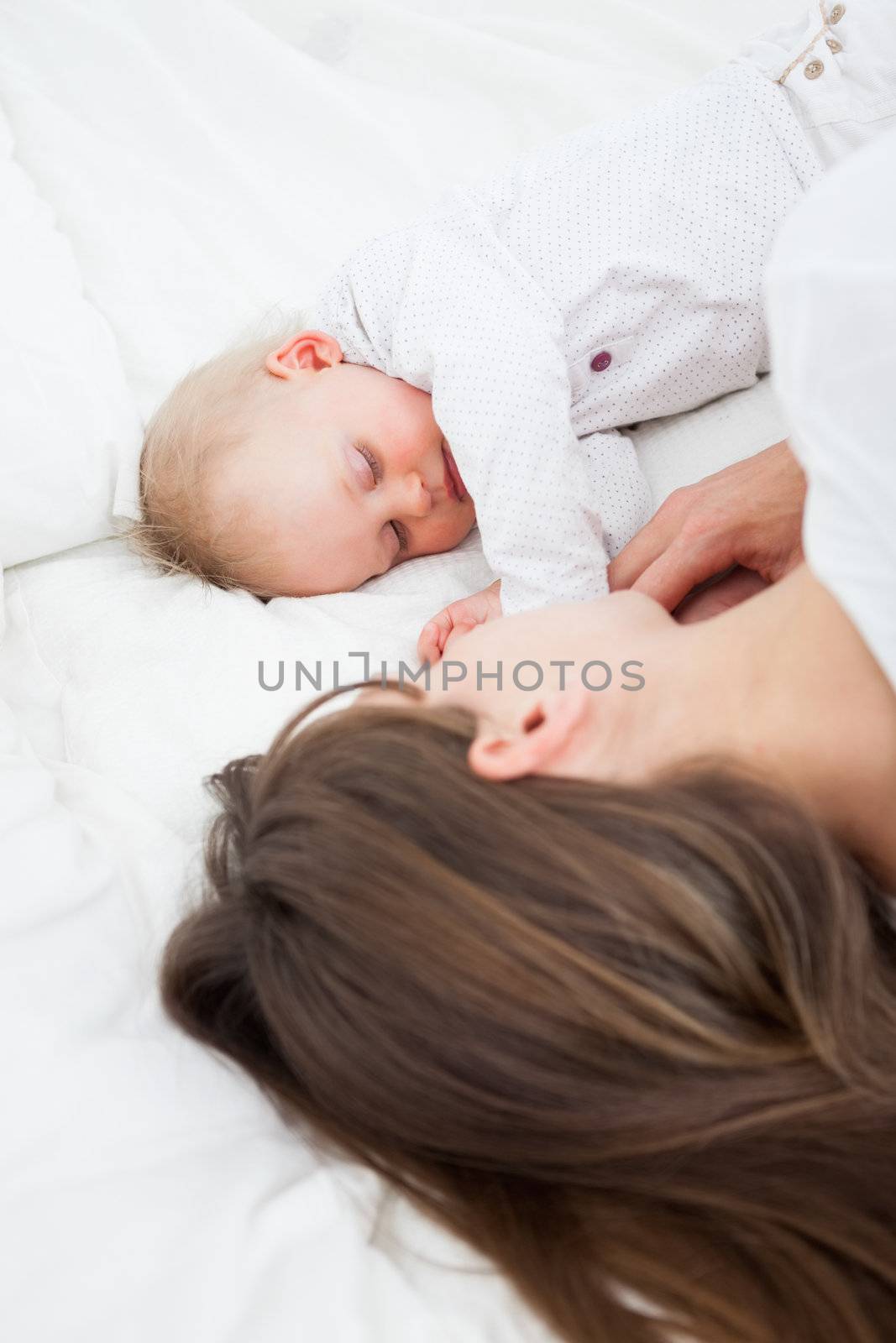 Brunette woman lying with her baby on her bed indoors