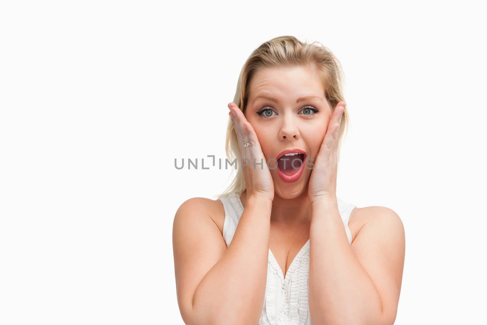 Surprised blonde woman putting her hands on her cheeks against a white background