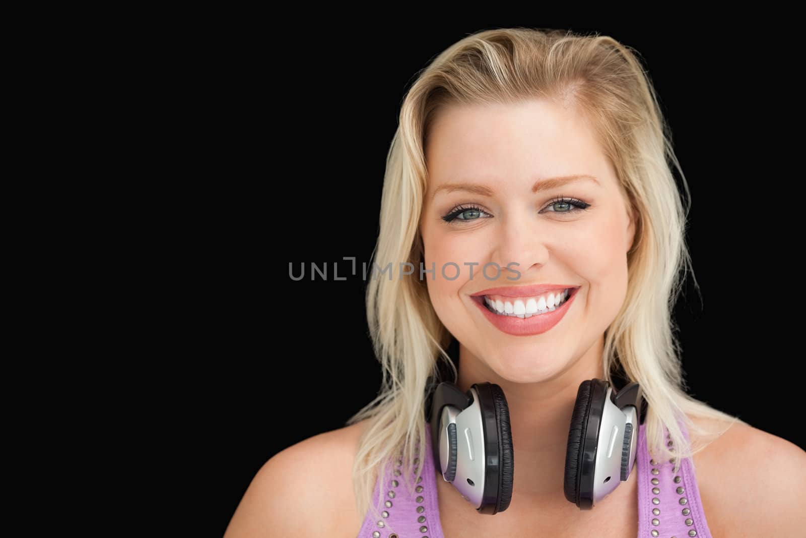 Happy blonde woman standing upright with headphones against a black background