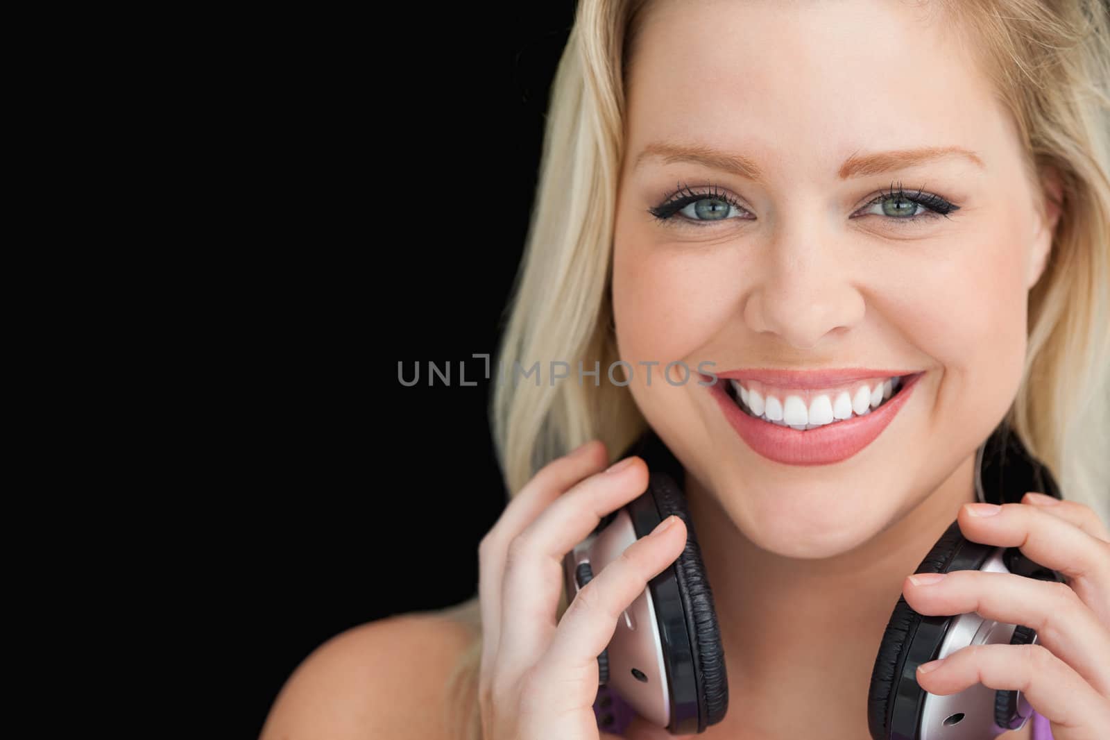 Smiling woman standing while holding her headphones against a black background