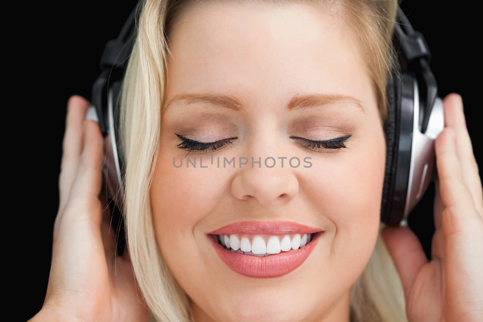 Cheerful woman closing her eyes while listening to music against a black background