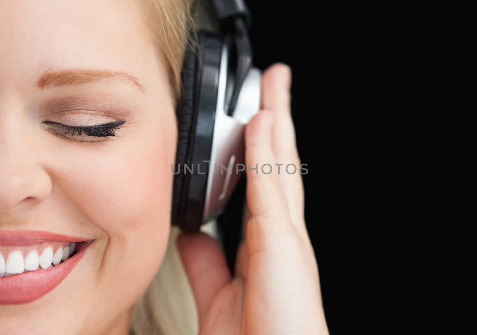 Joyful woman closing her eyes while listening to music against a black background