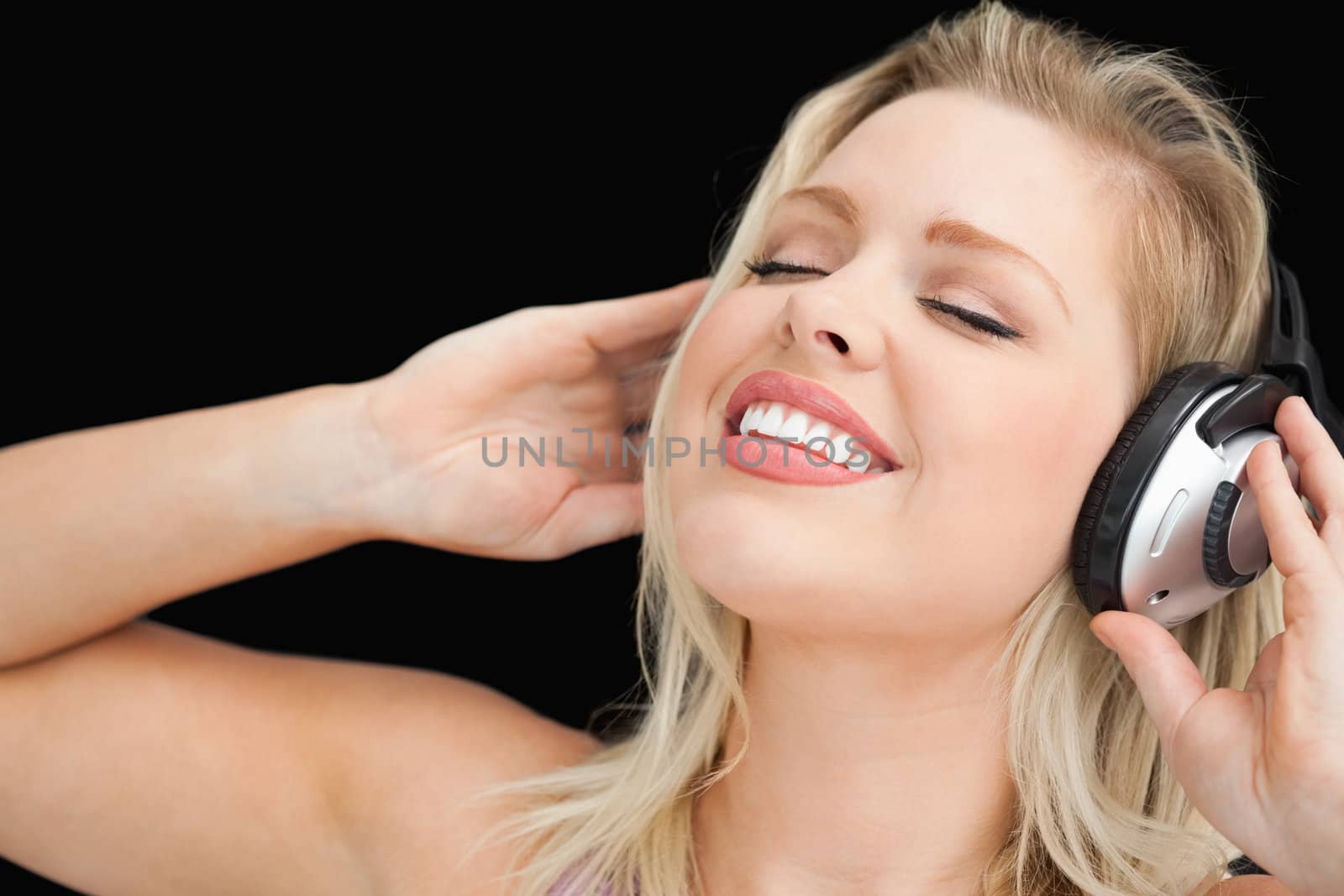 Joyful blonde woman listening to music through headphones against a black background