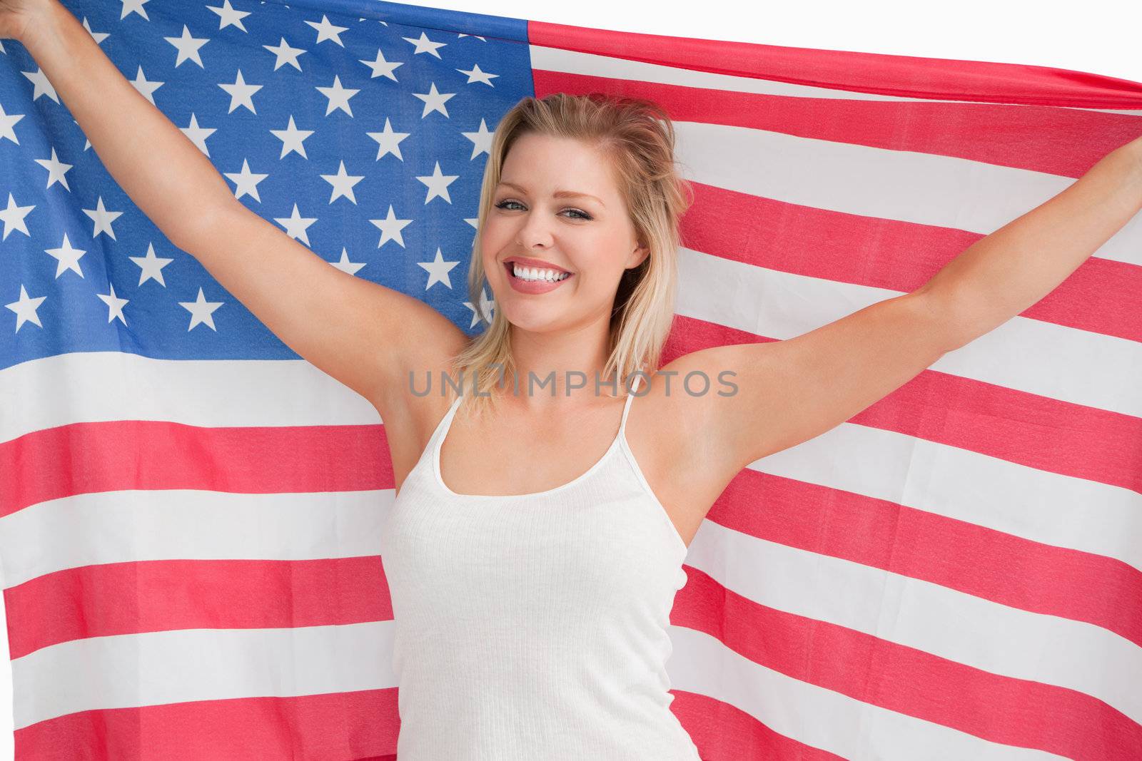 Joyful blonde woman holding the Stars and Stripes flag against a white background