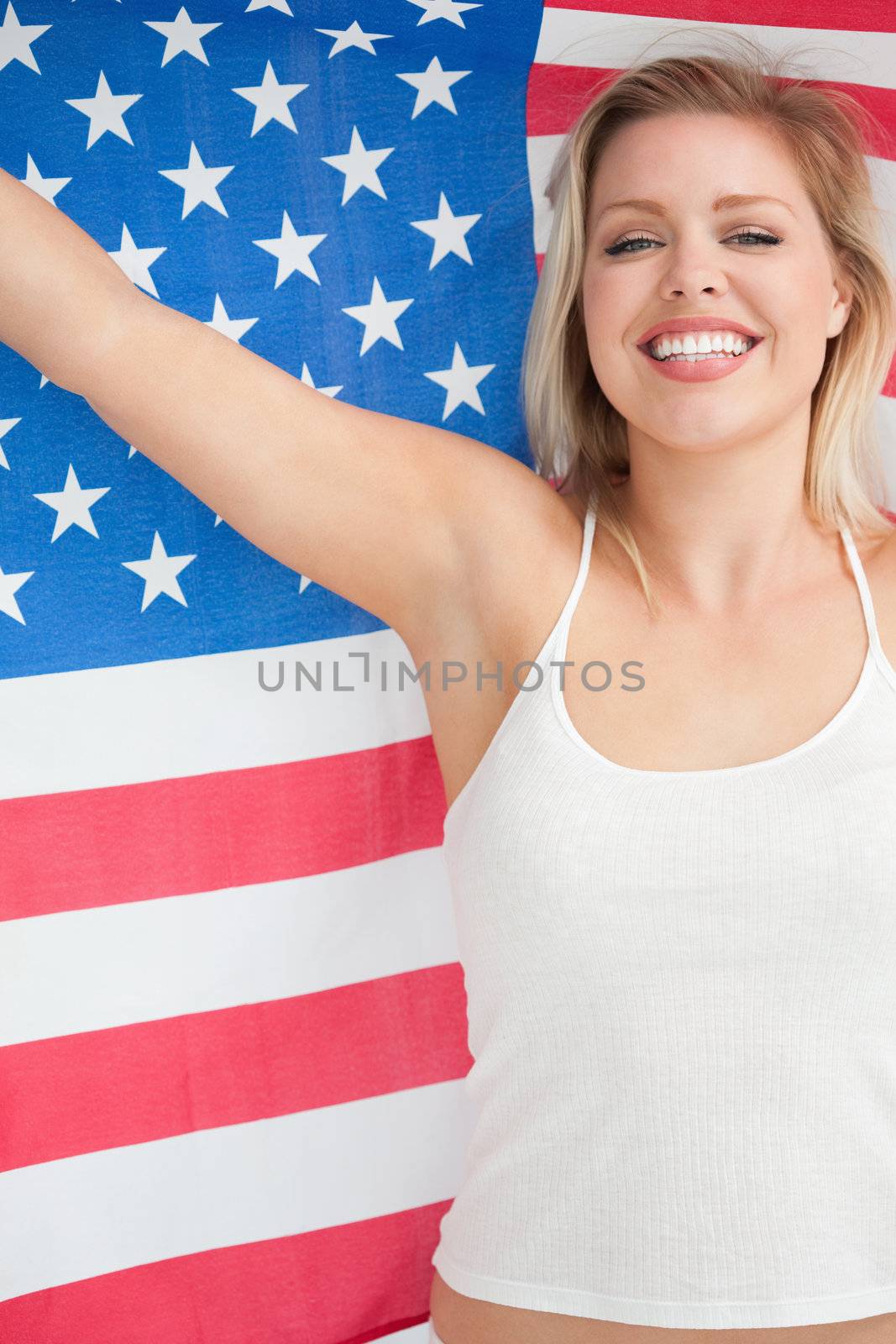 Cheerful blonde woman raising the Stars and Stripes flag in a studio