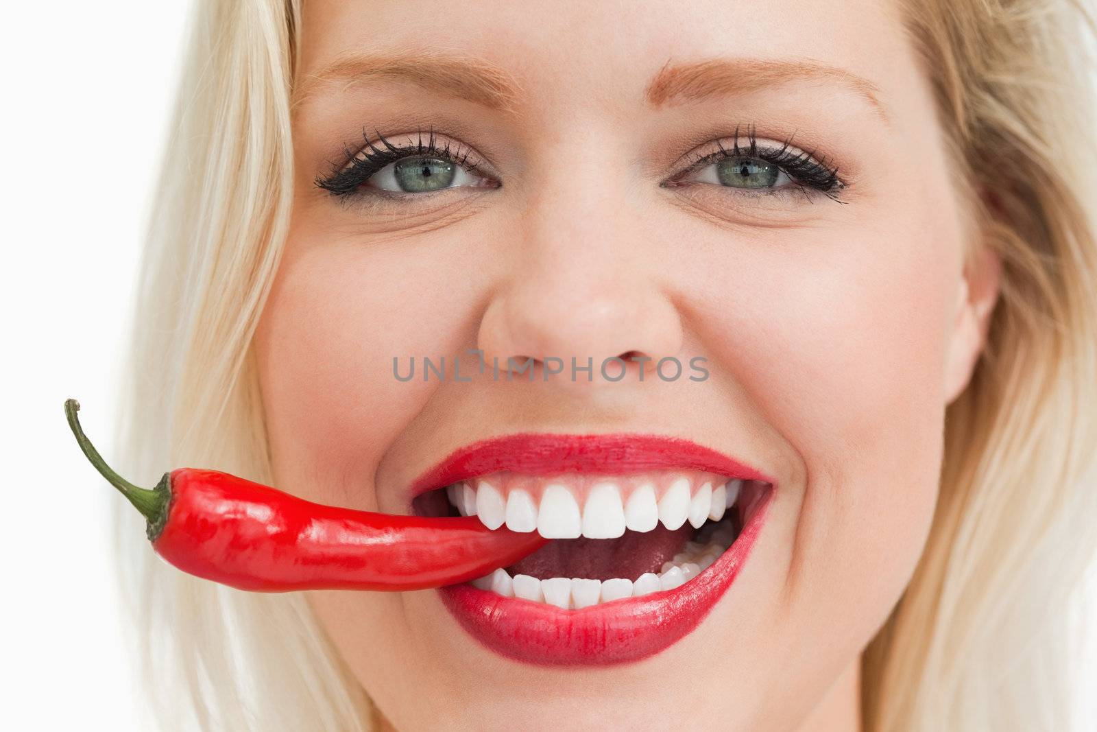 Happy blonde woman biting a red chili pepper against a white background