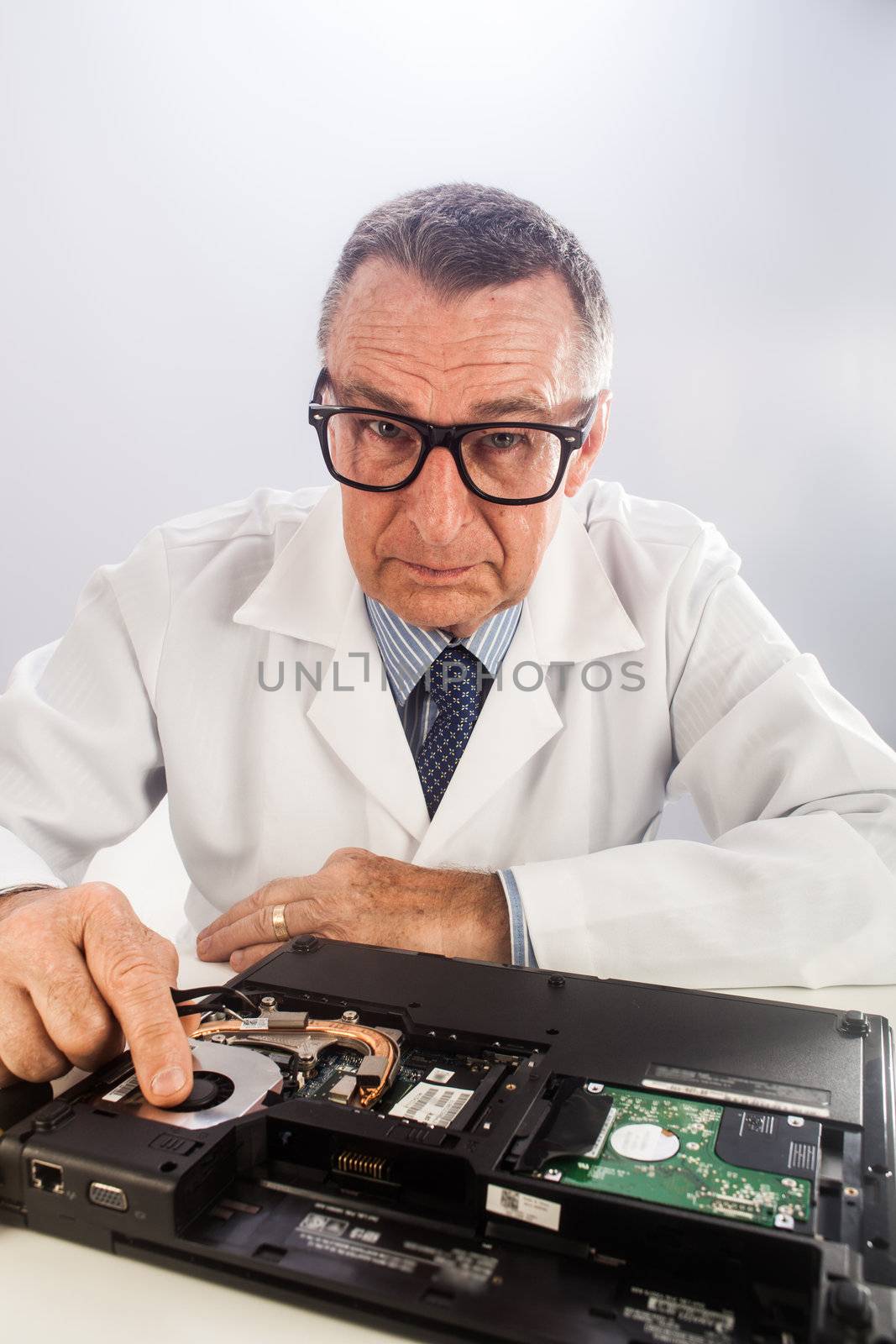 An older male wearing a white lab coat and reaparing electronic equipments, like a technician or a repair man.
