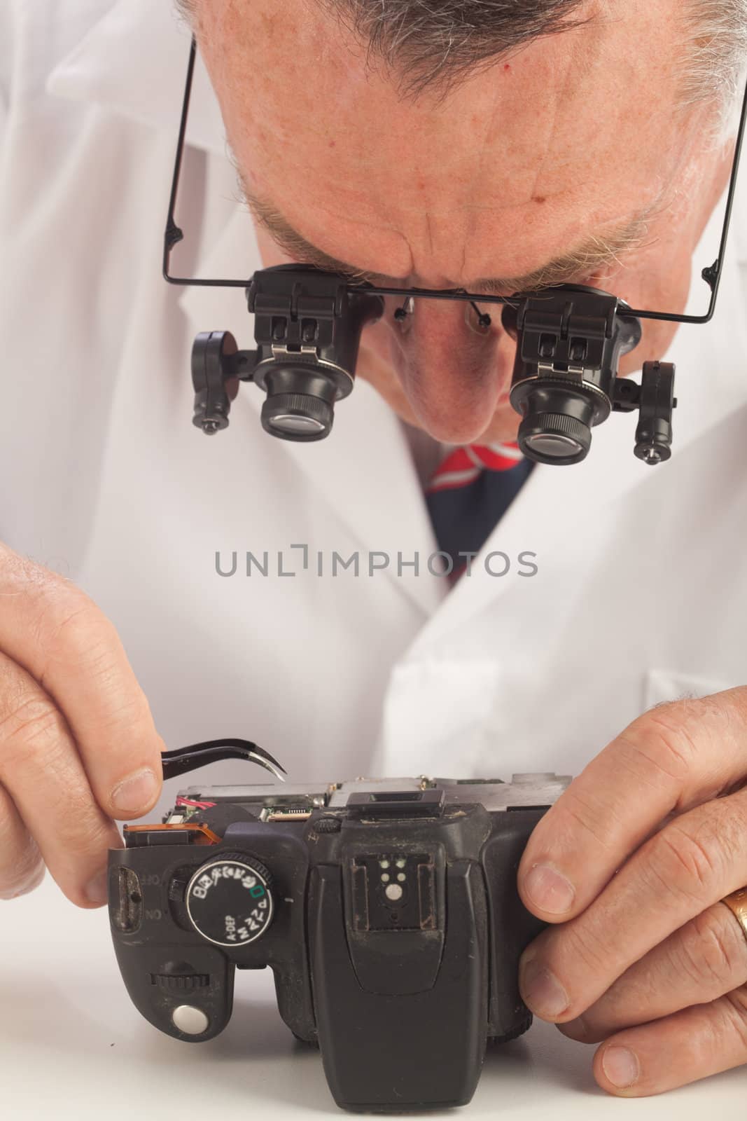 An older male wearing a white lab coat and reaparing electronic equipments, like a technician or a repair man.