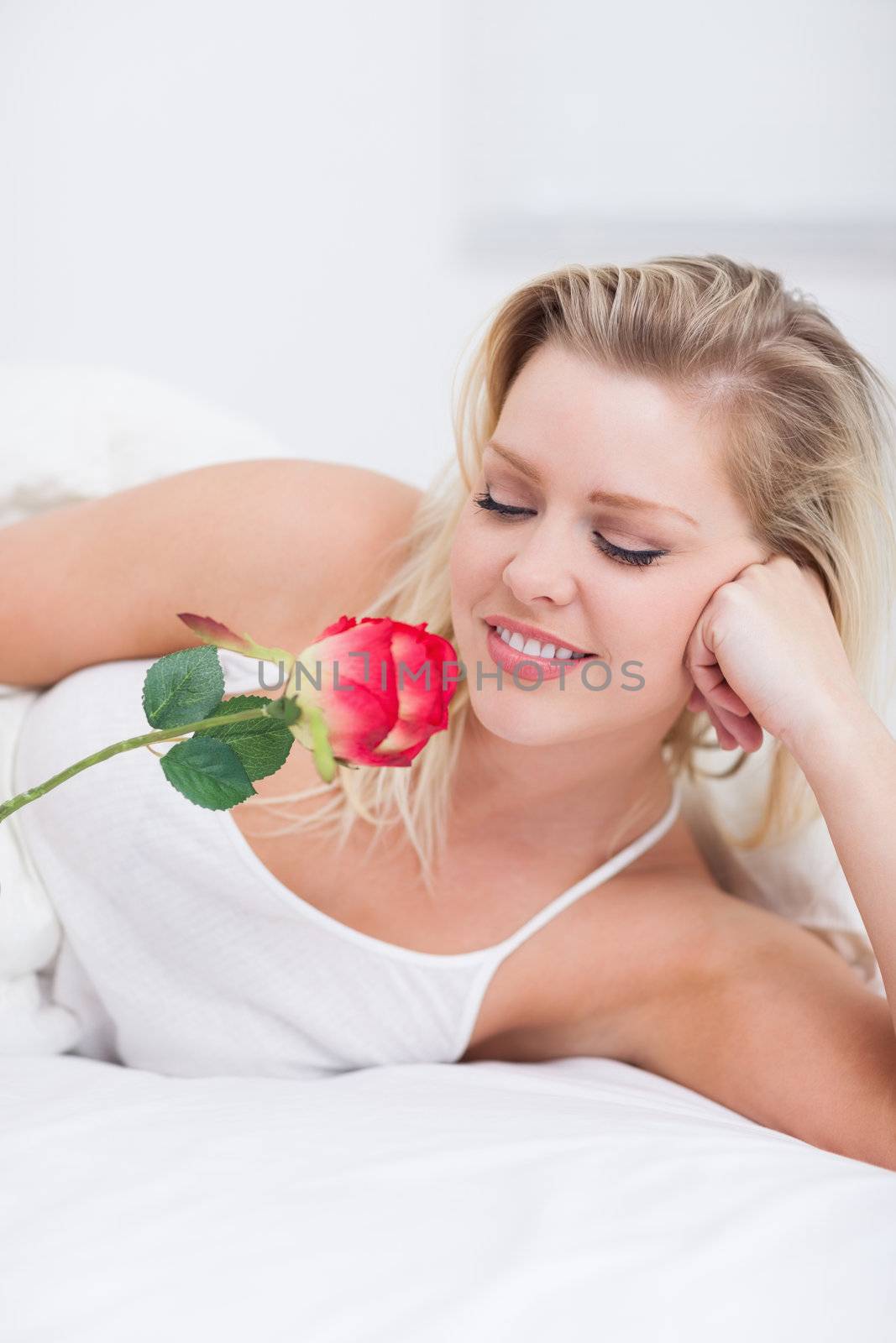 Young woman looking at her pink rose while lying on her bed